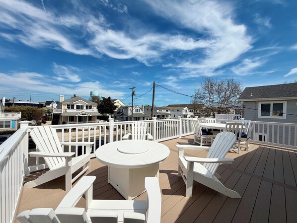 A deck with a round table and white Adirondack chairs, surrounded by a white railing.