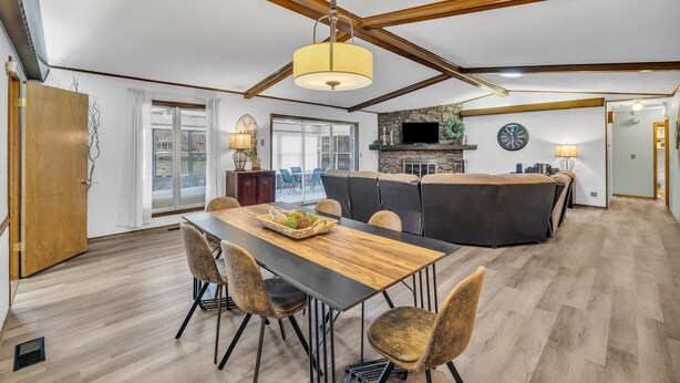 A spacious living area with a wooden dining table, comfortable seating, a fireplace, and a large window providing a view of the outdoors. - 4BR Retreat w/ KING Bed, Hot Tub & Prime Location (Owasso)