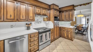 A kitchen with wooden cabinets, a stainless steel dishwasher, an oven, and a white countertop. - 4BR Retreat w/ KING Bed, Hot Tub & Prime Location (Owasso)