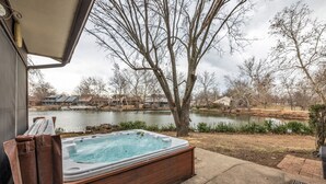 A hot tub with a wooden exterior, situated near a body of water and surrounded by trees and houses. - 4BR Retreat w/ KING Bed, Hot Tub & Prime Location (Owasso)