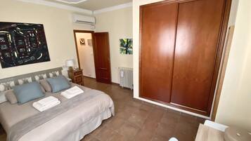 Habitación de hotel con cama, mesita de noche, equipo de aire acondicionado, radiador y un amplio armario de madera.