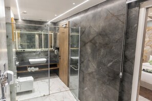 Un baño moderno con ducha de vidrio, tocador de madera y suelo de mármol.