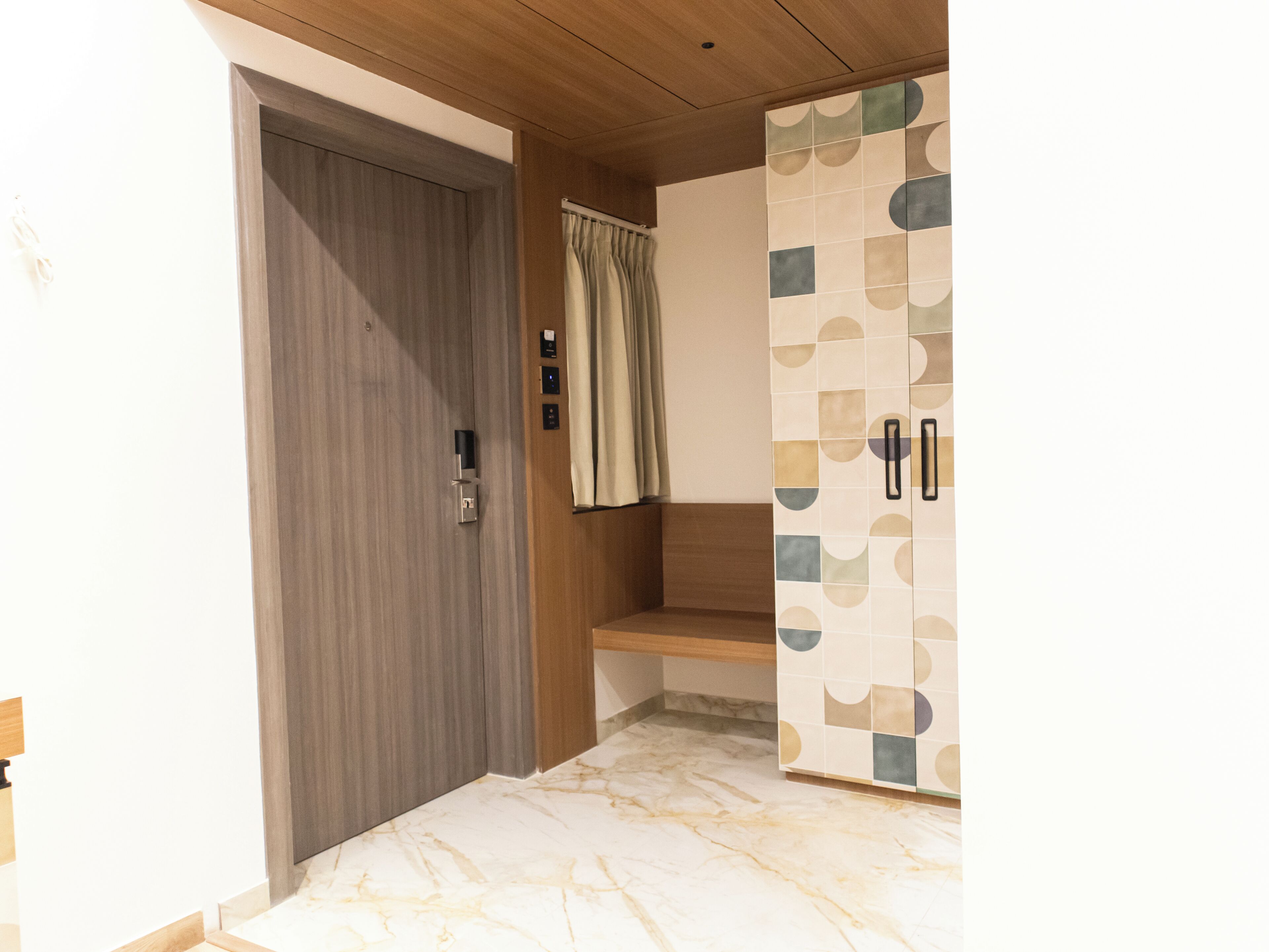 Une salle de bain avec une porte en bois, un espace douche séparé par un rideau et un mur recouvert de carreaux formant un motif géométrique.