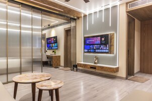 Un moderno vestíbulo de hotel con un televisor de pantalla plana grande mostrando un menú digital, una recepción y una zona de estar con dos mesas redondas.