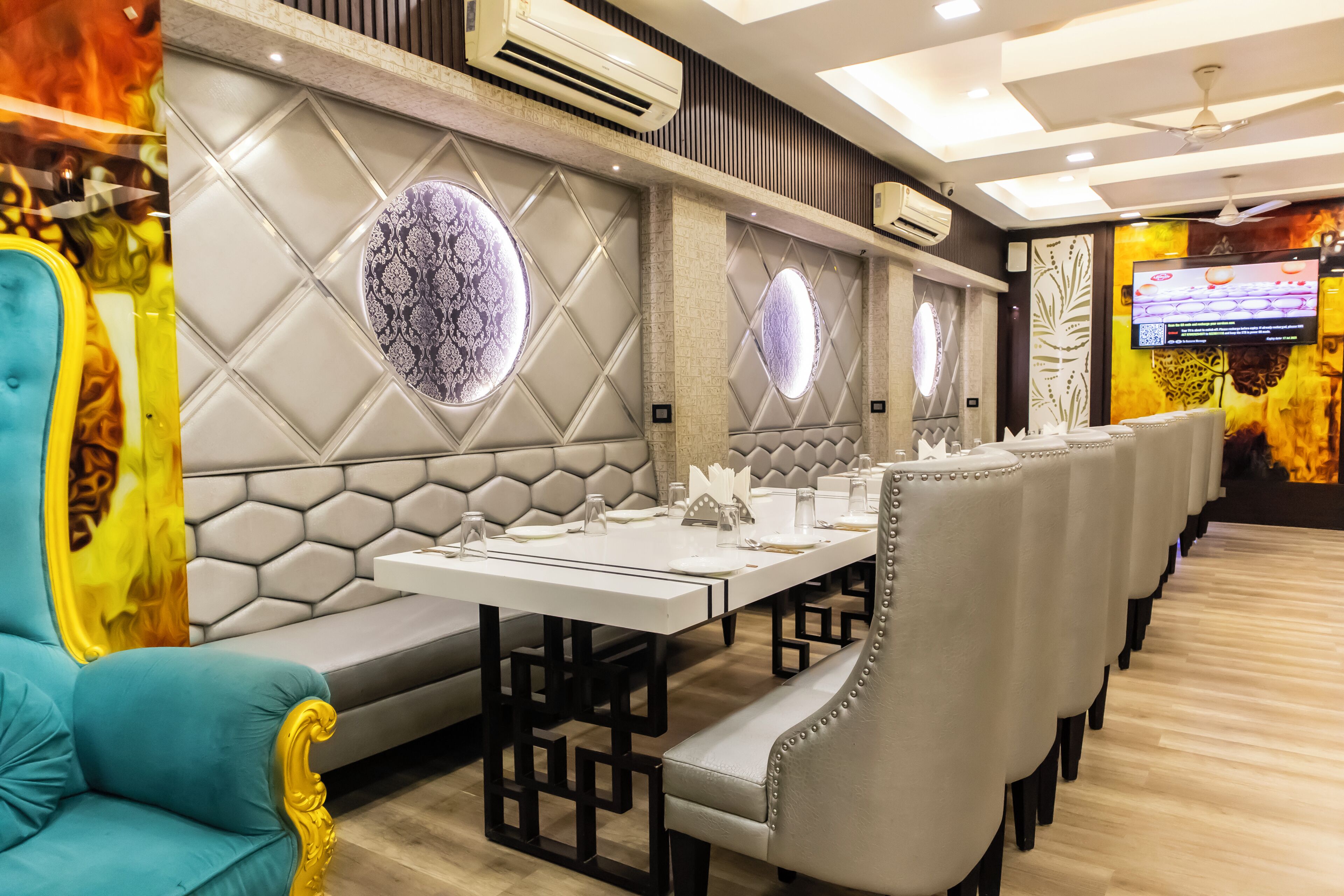 Un restaurant avec une longue table dressée pour le repas, des sièges rembourrés et des panneaux décoratifs sur les murs.