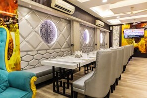 A restaurant with a long table set for dining, cushioned seating, and decorative wall panels. - Narang Hotel (Hanumangarh)