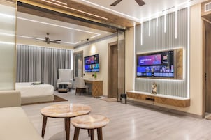 Habitación de hotel moderna con una televisión de pantalla plana grande montada en la pared, un sofá, un escritorio con una silla y una pequeña mesa con dos taburetes.