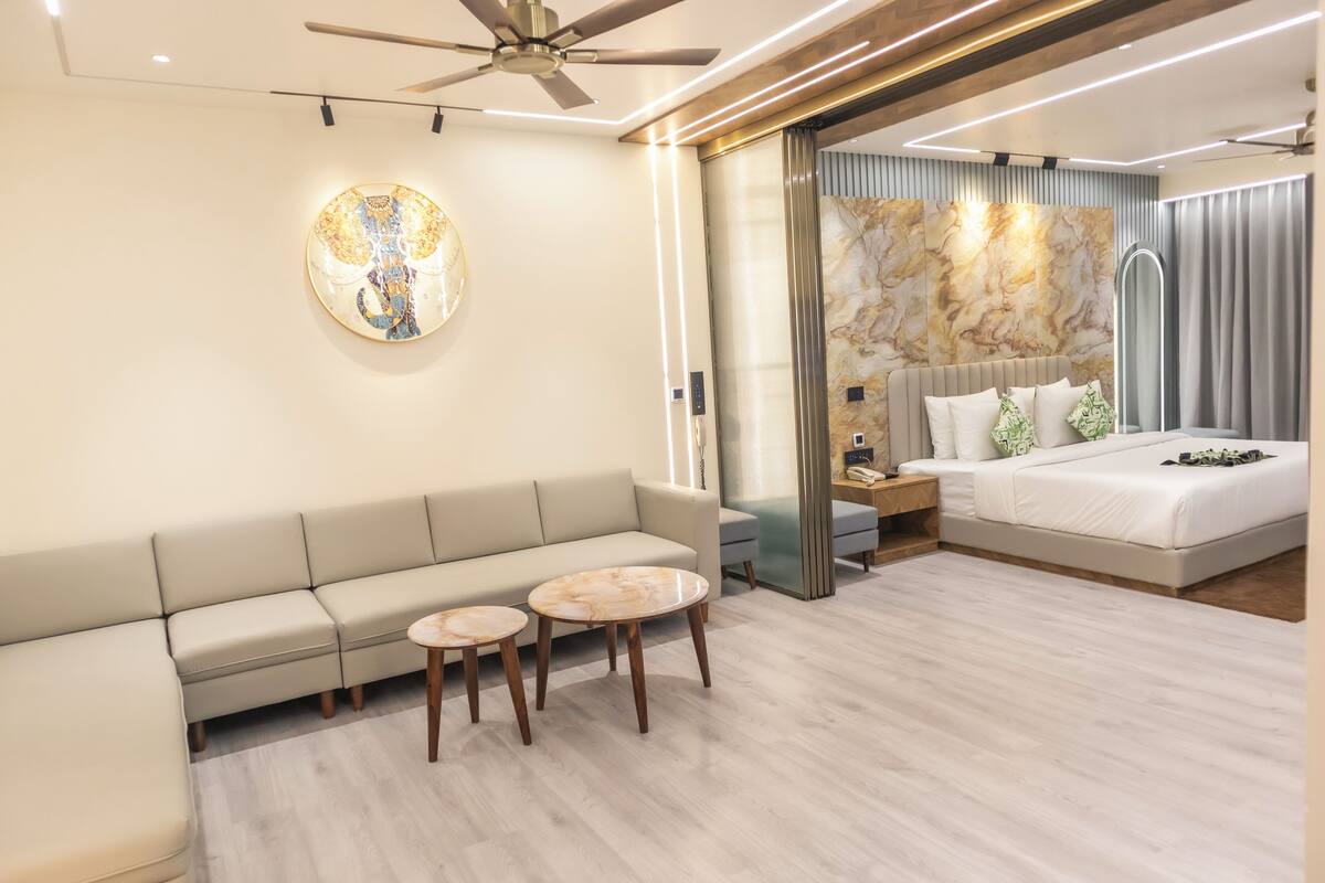 Ein modernes Hotelzimmer mit einer Couch, zwei runden Tischen, einem Bett mit Kopfteil und einem Deckenventilator.