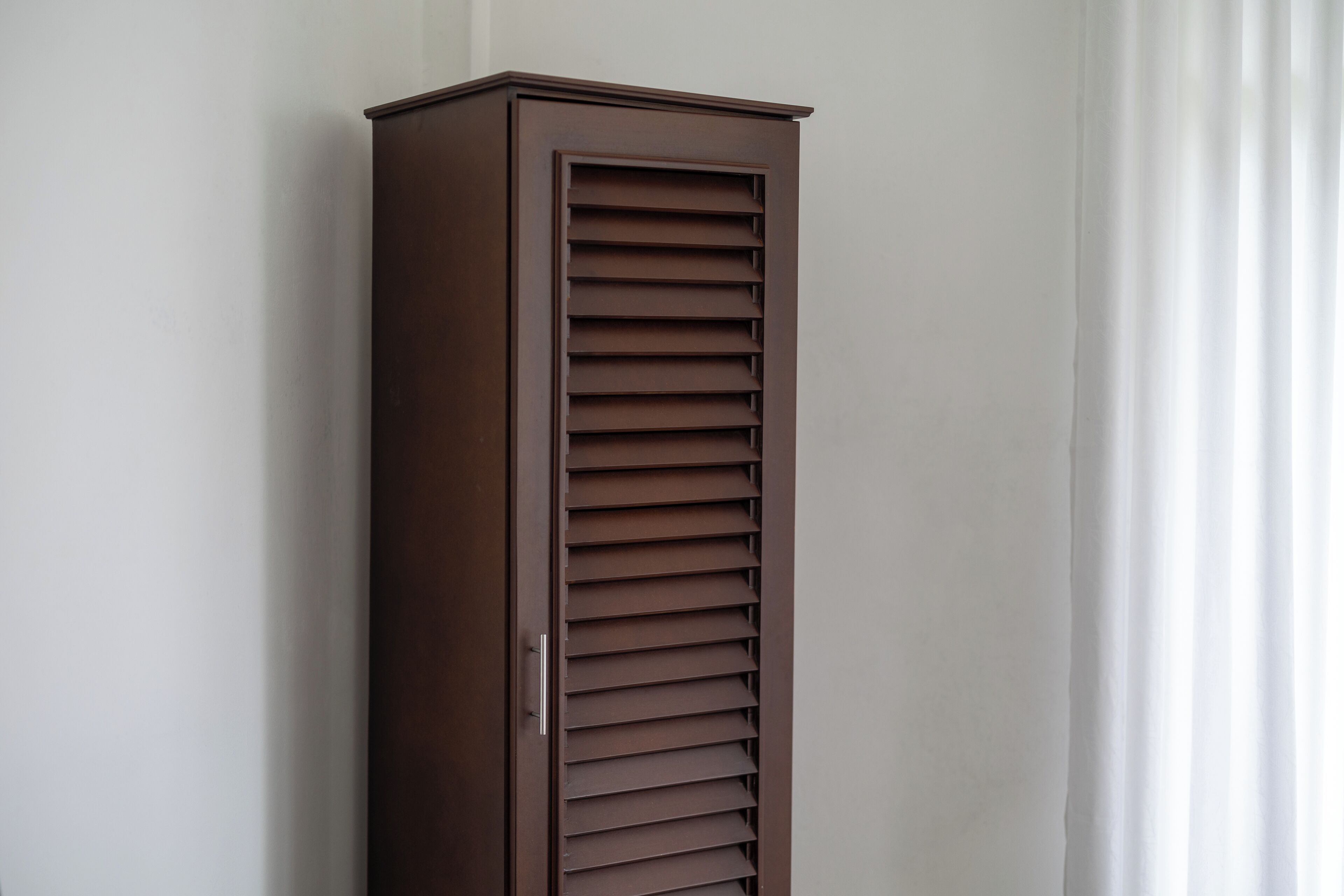A tall, narrow wardrobe with horizontal slats, a handle, and a flat top.