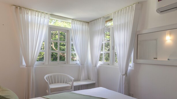 A bedroom with a bed, a chair, and two windows with curtains. - Greenwood Edge Kandy (Kandy)