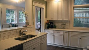 Una cocina con armarios blancos, un lavamanos doble y una ventana con vistas a zonas verdes.
