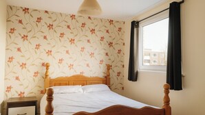 A bedroom with a wooden bed, a nightstand, a window with curtains, and floral wallpaper. - 3br-sleeps5-balcony-centrallondon-ws95 (London)