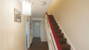 A hallway with a wooden floor, a red and white staircase, a chandelier, and a door at the end. - 3br-sleeps5-balcony-centrallondon-ws95 (London)
