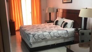 A hotel room with a bed, two bedside lamps, a framed picture on the wall, and a window with orange curtains. - AMSY HOTEL AMSY HOTEL (Dakar)