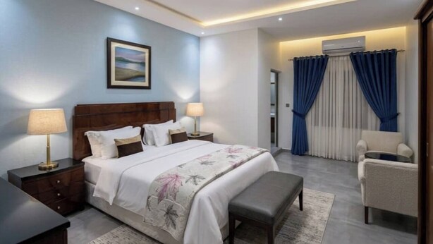 A bedroom with a bed, bedside tables, a bench, a chair, and a view of a balcony with curtains. - AMSY HOTEL AMSY HOTEL (Dakar)
