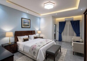 A bedroom with a bed, bedside tables, a bench, a chair, and a view of a balcony with curtains. - AMSY HOTEL AMSY HOTEL (Dakar)