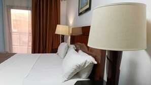 A hotel room with a bed, two bedside lamps, a window with curtains, and a framed picture on the wall. - AMSY HOTEL AMSY HOTEL (Dakar)