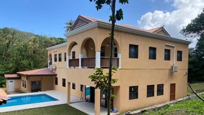 A two-story building with a swimming pool, a covered patio, and a view of a hilly landscape.