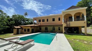 A two-story building with a swimming pool, outdoor seating, and a covered patio area.