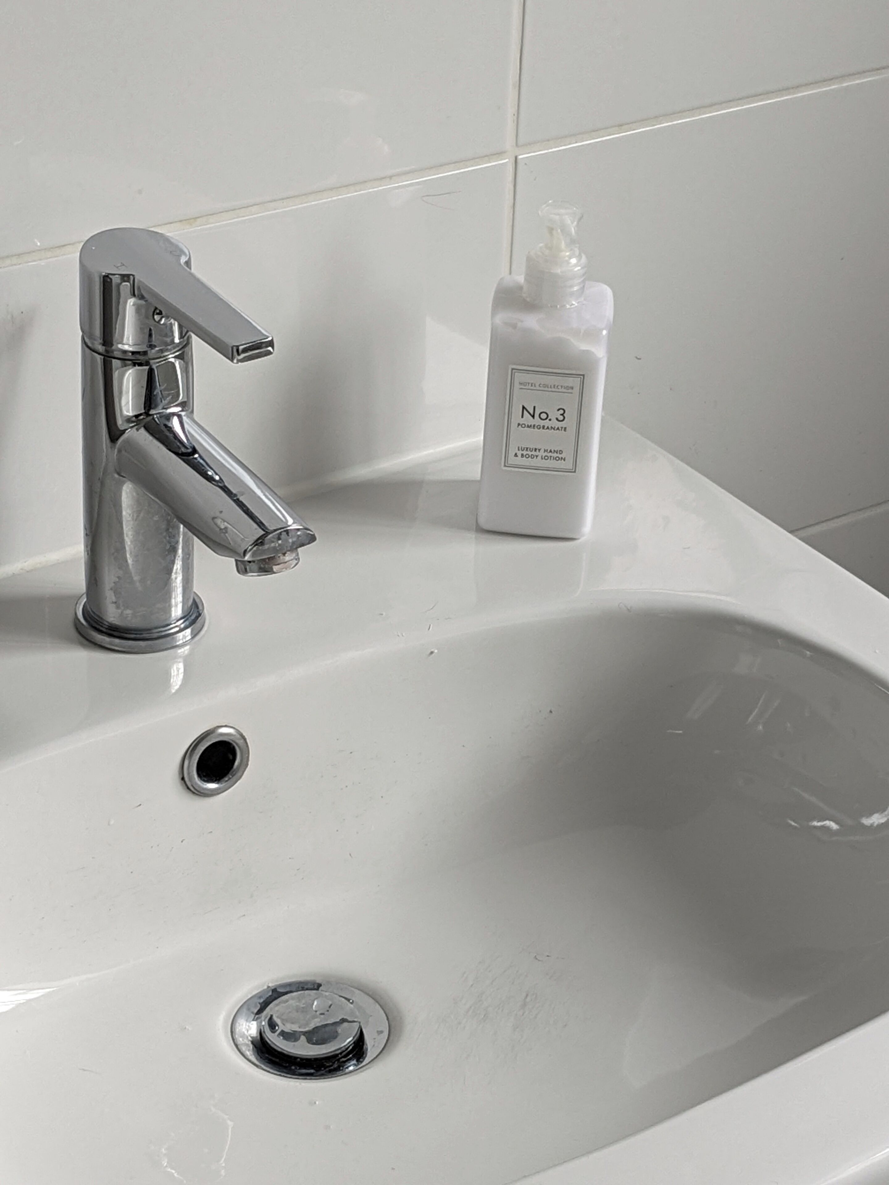 A bathroom sink with a chrome faucet and a bottle of Hotel Collection No. 3 Pomegranate Luxury Hand & Body Lotion.