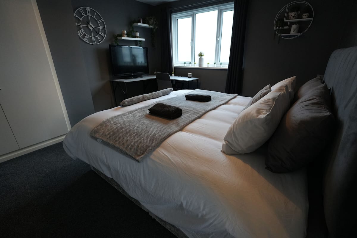 A bedroom with a large bed, a desk, a television, and a window with a view.