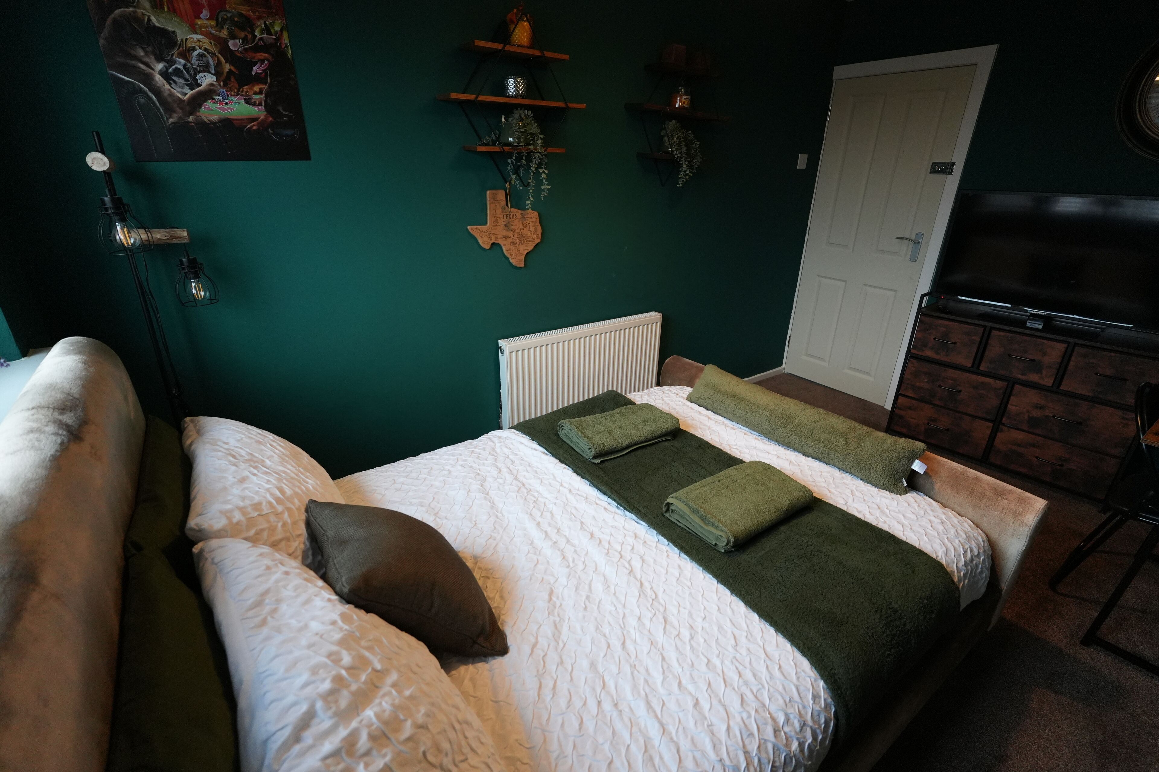 Une chambre à coucher avec un lit, des oreillers, un radiateur, une porte et des étagères ornées d’objets décoratifs.