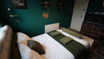 Une chambre à coucher avec un lit, des oreillers, un radiateur, une porte et des étagères ornées d’objets décoratifs.