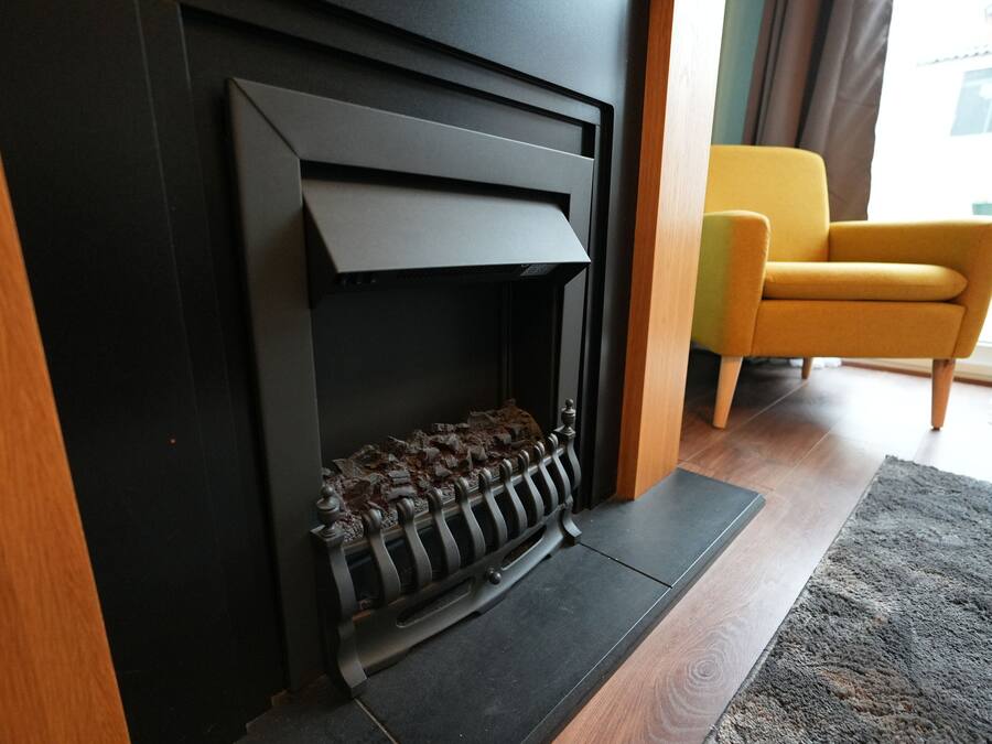 A modern fireplace with a black mantel, a wooden floor, and a yellow armchair.
