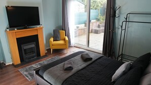 Quarto com cama, televisão, lareira, poltrona amarela e vista para o exterior.