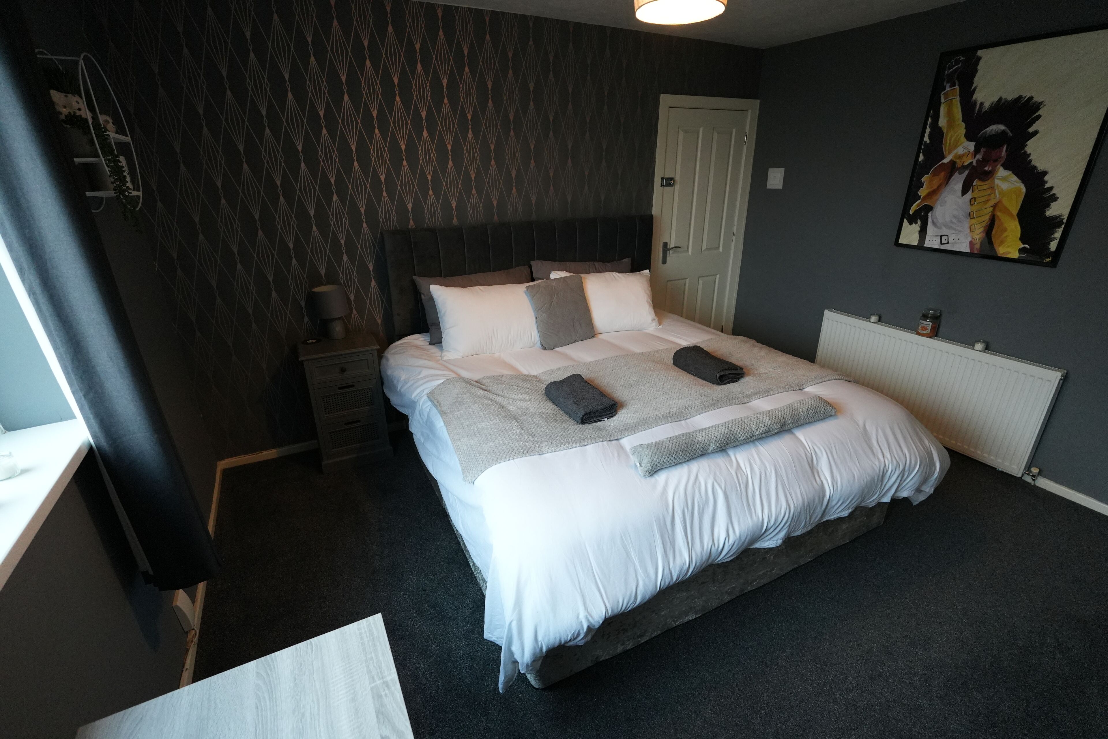Un lit bien fait, avec une couette grise et blanche, une table de chevet avec une lampe et un tableau accroché au mur.