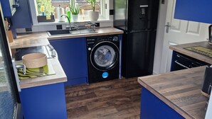 Cozinha compacta com máquina de lavar, geladeira e janela com vista para uma área residencial.