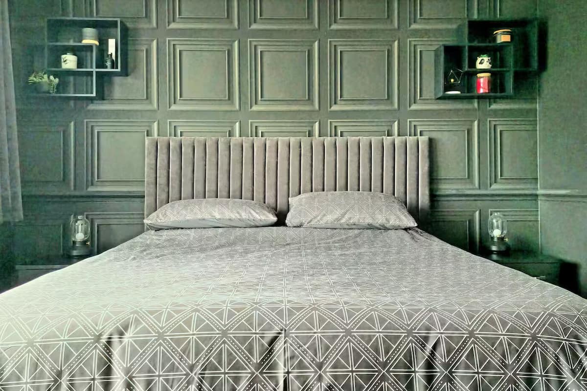A bed with a geometric patterned bedspread, a tufted headboard, and two matching pillows. There are bedside tables with lamps and wall-mounted shelves with decorative items.