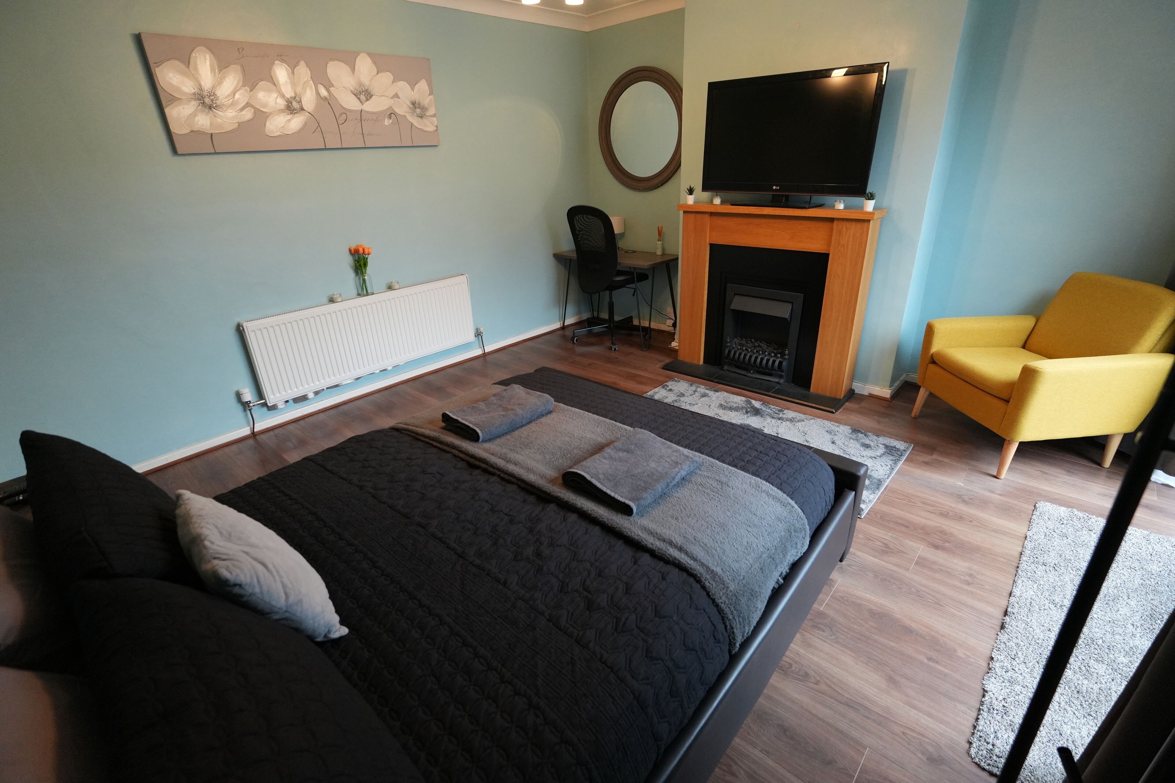A modern bedroom with a large bed, a TV, a fireplace, and a yellow armchair.