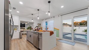 A modern kitchen with a central island, stainless steel appliances, pendant lighting, and a view of a backyard with a pool.
