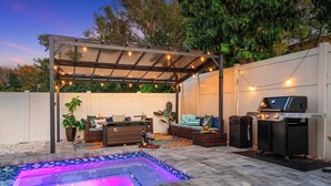 An outdoor patio with a swimming pool, a covered seating area, and a barbecue grill.