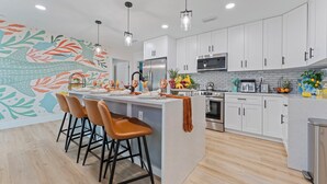 A modern kitchen with white cabinets, a central island with bar stools, and a colorful wall mural.