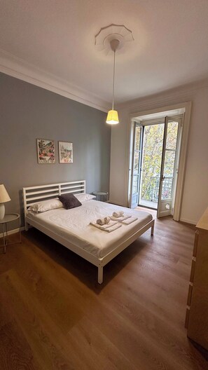 A bedroom with a bed, a bedside table, a lamp, a ceiling light, and a window with a view of trees. - Stay in Milan's trendiest street (Milano)