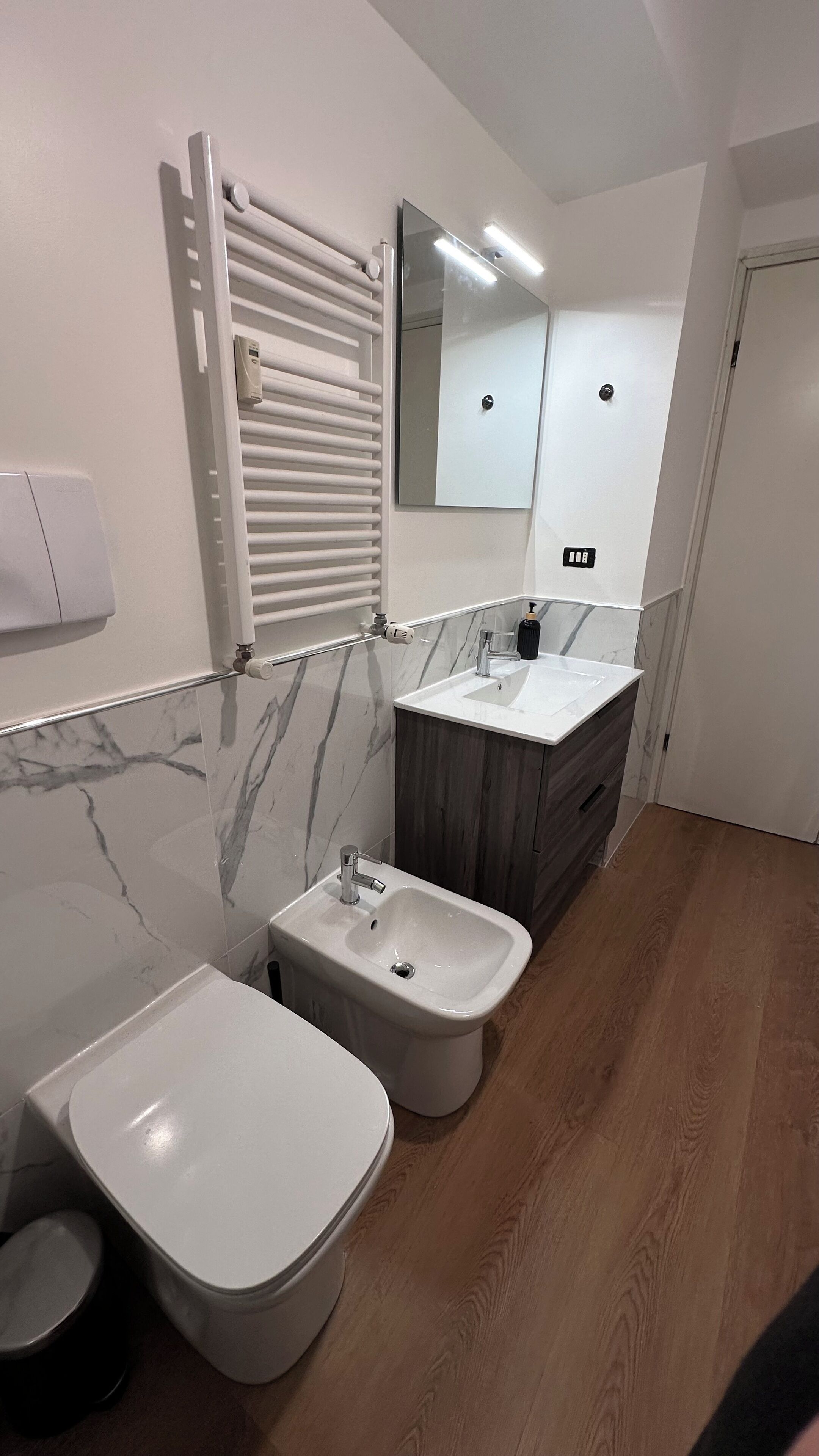 Een moderne badkamer met toilet, bidet, wastafel met spiegel en een handdoekhouder.