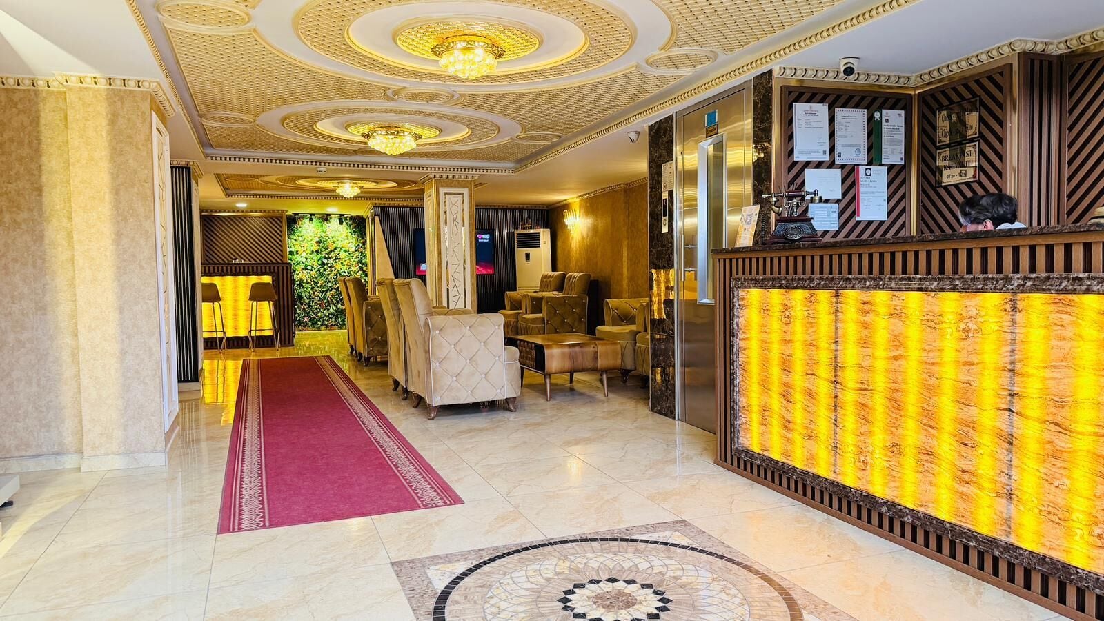 A hotel lobby with a red carpet, a reception desk, and a wall with vertical lines.