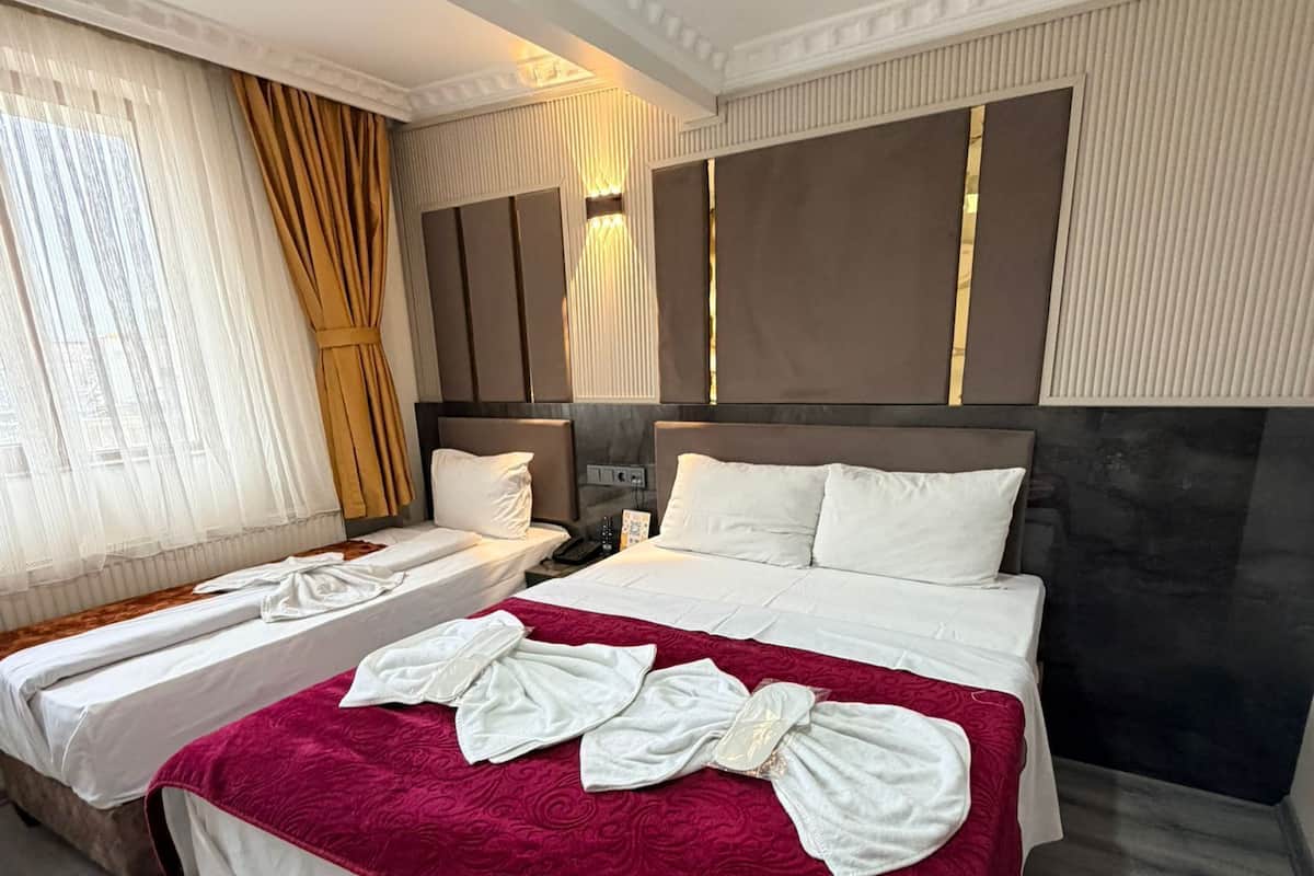 A hotel room with two beds, a red blanket, a large mirror, and a ceiling light.
