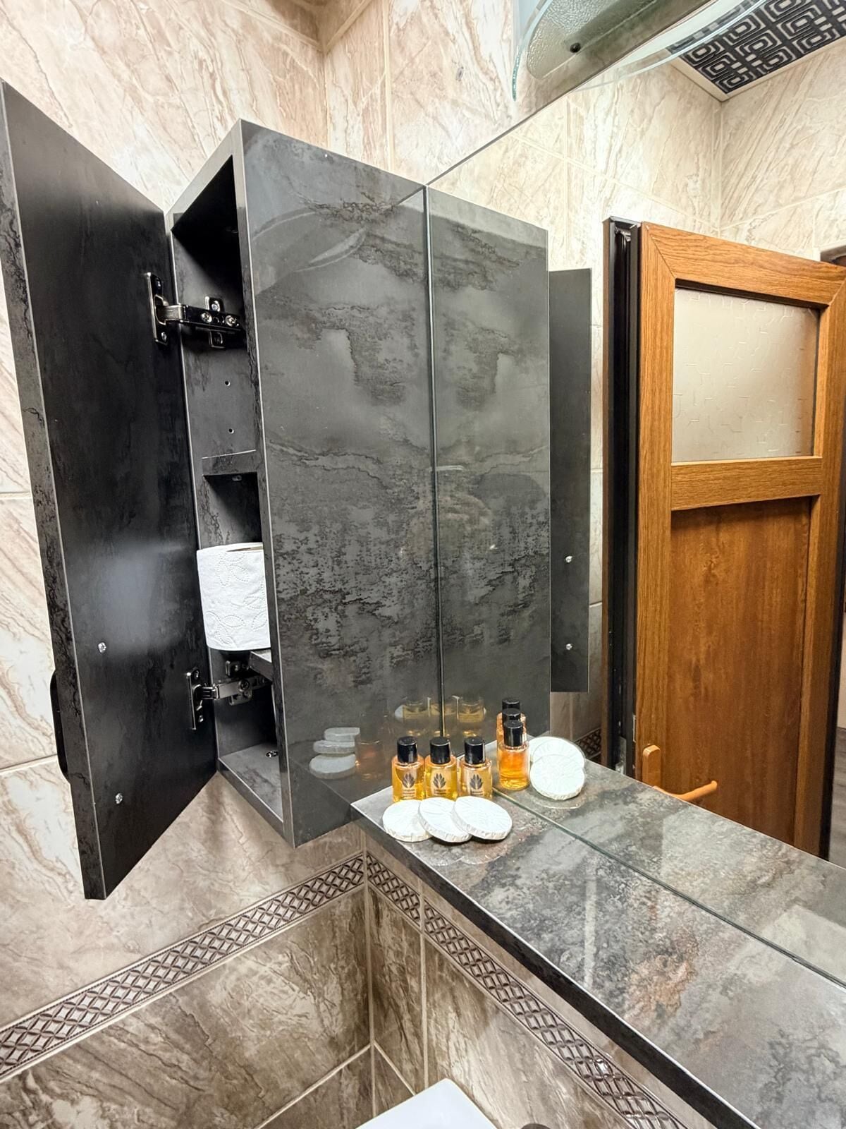 A bathroom with a marble vanity, a wooden door, and toiletries on the counter.