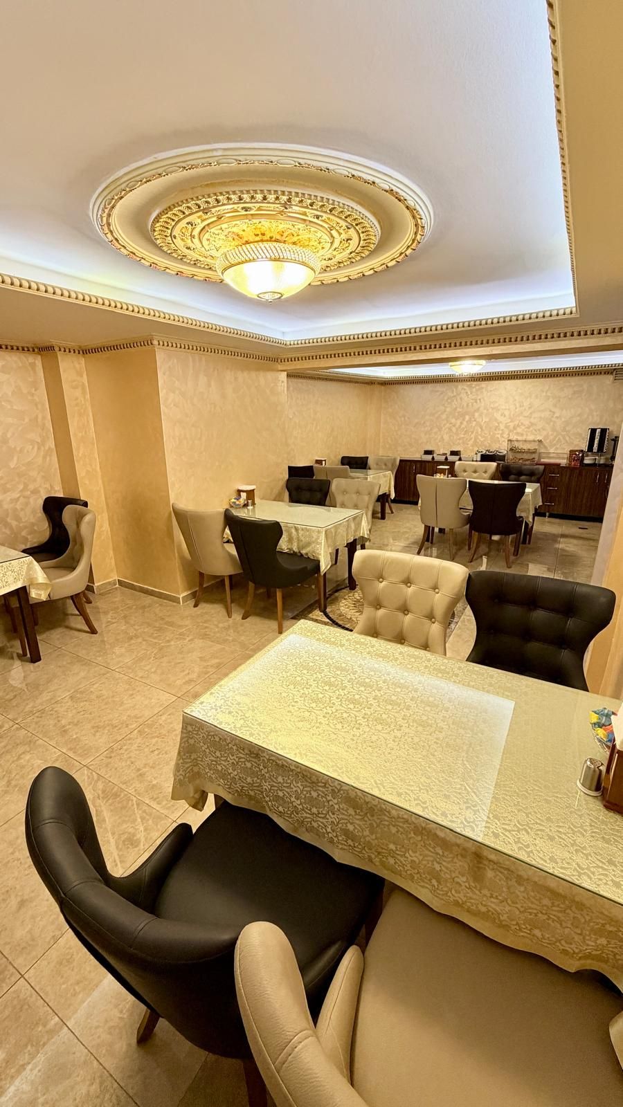 A dining area with tables and chairs, a decorative ceiling, and a patterned floor.