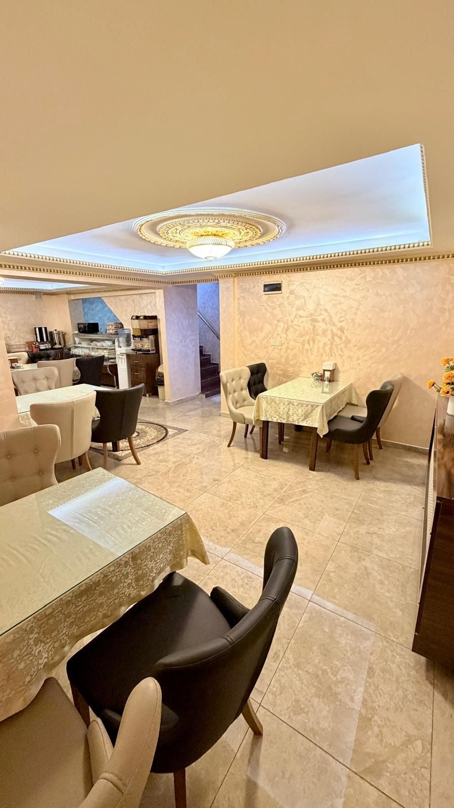 A hotel dining area with a central table, surrounding chairs, and a kitchen in the background.