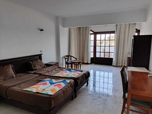 Quarto de hotel com duas camas, uma escrivaninha, uma cadeira e uma janela grande com cortinas.