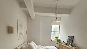 A bedroom with a bed, a dresser, a nightstand, a window, and a hanging light fixture. - Charming 2-bedroom Tribeca apartment with views (New York)