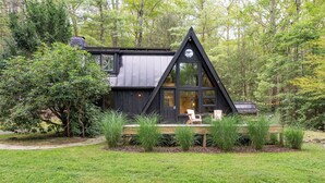 Una cabaña con techo triangular, ventanas amplias y una terraza con sillas.