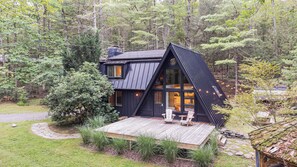 Una cabaña moderna con techo inclinado, ventanas amplias y una terraza de madera.