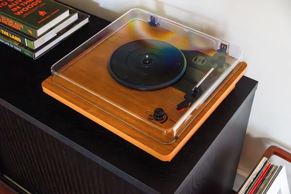 Tocadiscos con cubierta transparente, una pila de libros y una superficie de madera.
