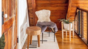Interior de madera con techo alto, una silla blanca, un taburete pequeño de madera y una planta en maceta.