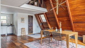 Un comedor con mesa y sillas de madera, una lámpara decorativa en el techo y vistas a la cocina y el espacio de estar.
